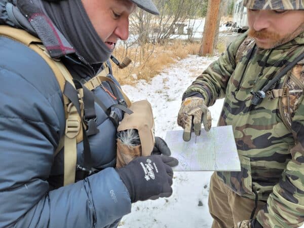 Two individuals in outdoor gear examining a map in a snowy environment.