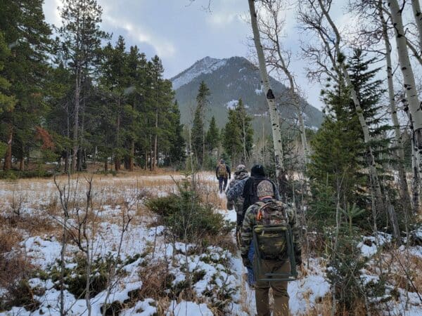 Hikers with backpacks trekking through a snowy forest toward a mountain.